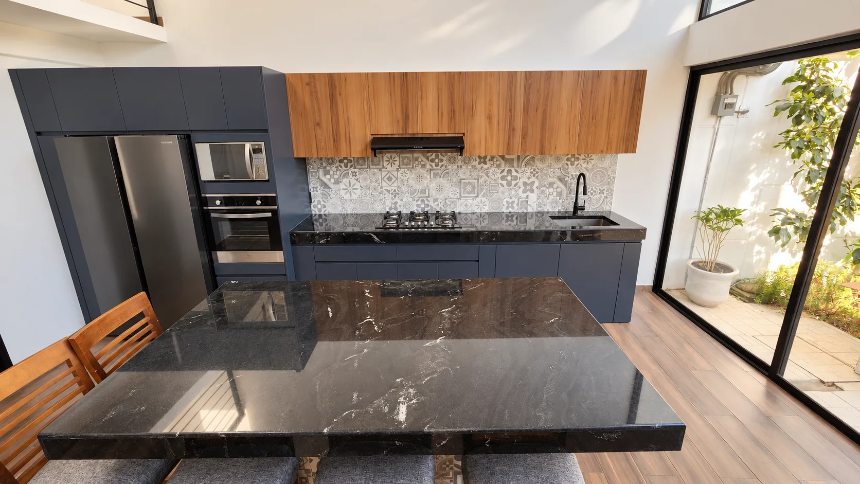 Cocina abierta con gabinetes azul profundo, madera natural, cubierta de piedra y mesa integrada