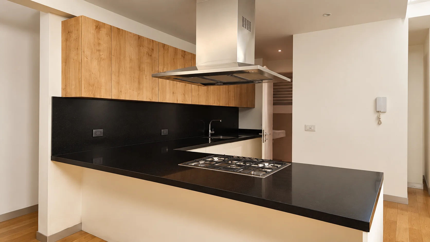 Cocina a medida con carpintería de madera, cubierta negra y campana de acero